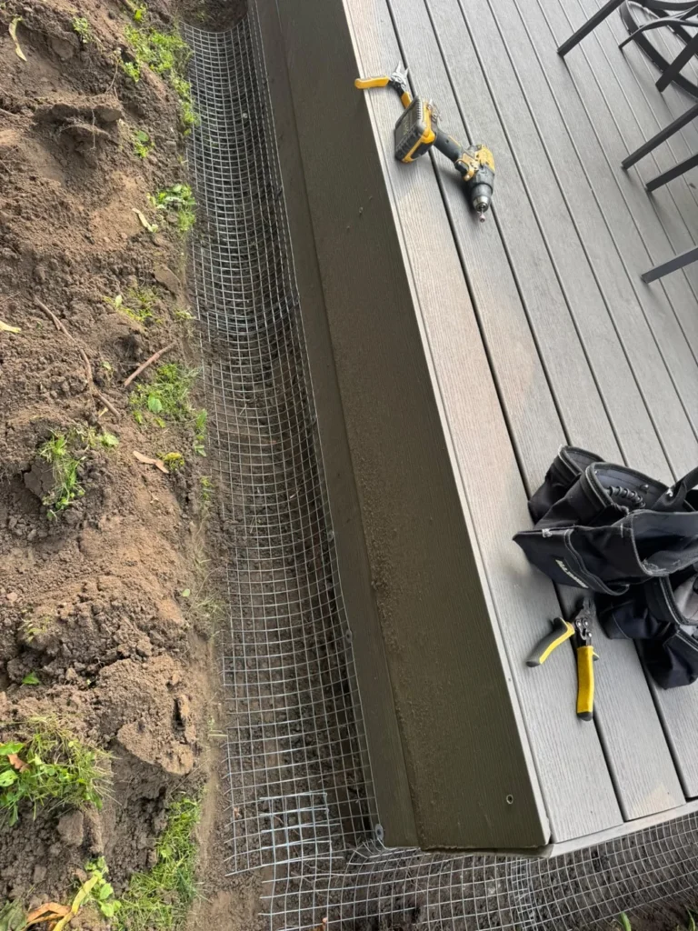 Buried-mesh exclusion work around a deck corner, shown during installation.