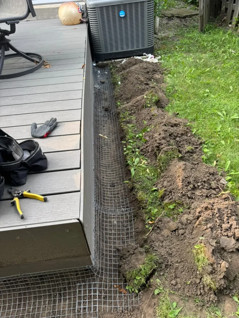 Wildlife exclusion mesh installed along a deck perimeter before backfilling.